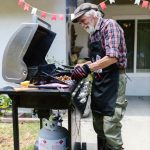 elderly man tending to meat gas grill